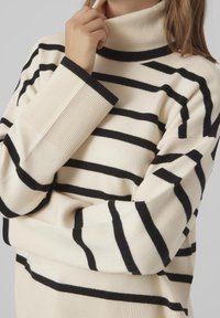 Sweter z golfem w paski w kolorze kremowym i czarnym, z prążkowanymi mankietami i kołnierzem, charakteryzujący się miękką teksturą i luźnym krojem.