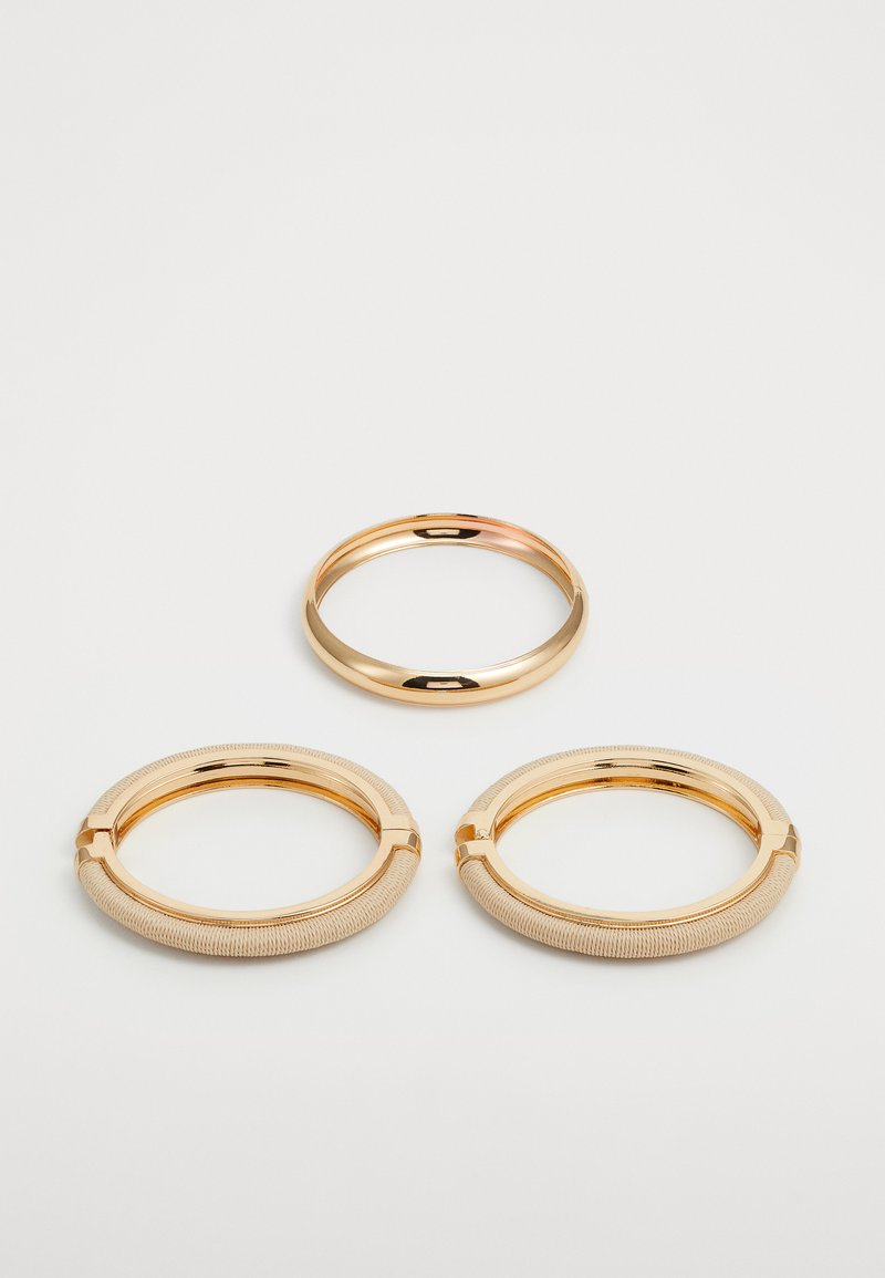 Smykke sett i gullfarge som inkluderer to teksturerte armbånd og en glatt ring, med blanke metalliske overflater og sirkulære former.