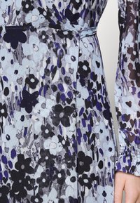 Kwiatowa sukienka w jasnoniebieskim materiale z czarnymi i fioletowymi kwiatami oraz strukturalnym wzorem, z długimi rękawami i dopasowaną talią z wiązaniem z boku.