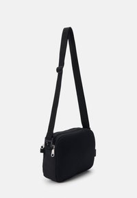 Kompaktní černá crossbody taška s nastavitelným popruhem a síťovanou přední částí, se stříbrnými zipy a detailem na přezce.