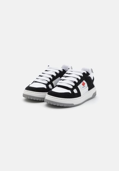 Zapatillas en blanco y negro con un diseño de ante y malla, que cuentan con una suela de goma gruesa y cordones blancos prominentes. Detalle del logo rojo en el costado.