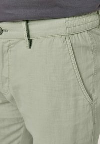 Hellgrüne Leinenhosen mit elastischem Bund, Vordertaschen und sichtbaren Steppnähten. Glattes, strukturiertes Gewebe.