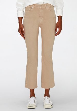 Beige cropped flare broek met rafelige zomen, gedragen met witte sneakers en een wit shirt met lange mouwen, voorkant zichtbaar.