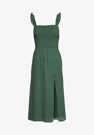 Vestido verde con lunares blancos, tirantes finos, acentos de volantes, corsé ajustado, falda fluida y una abertura frontal. Tejido ligero.