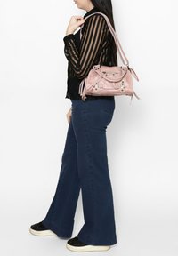 Borsa in suede rosa con hardware metallico e dettagli in frange, portata da una persona che indossa una maglietta a righe nera e jeans a zampa d'elefante blu.