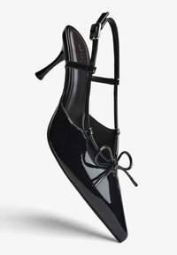Čierna lakovaná kožená dámska lodička na vysokom podpätku so špicatou špičkou, prackou za pätou a dekoratívnou mašľou vpredu. Hladká textúra a elegantný dizajn.