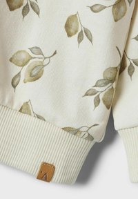Sudadera de color crema claro con un patrón floral en tonos verdes y amarillos apagados. Puños acanalados y una etiqueta de cuero marrón con el detalle de una 'A'.