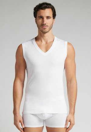 Weißes ärmelloses Unterhemd mit V-Ausschnitt, aus glattem Stoff gefertigt. Getragen mit passenden weißen Shorts, die eine figurschmeichelnde Silhouette zeigen.
