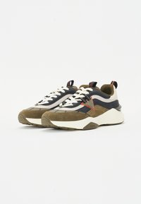 Olíva zöld velúrból, tengerészkék szövetből és fehér kiegészítőkből készült sneaker. Lapos bézs cipőfűzőkkel és tömör fehér talppal rendelkezik, márkázott részletekkel.