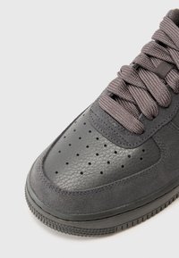 Dark gray sneaker with leather and suede materials, round toe, perforations on the upper, and textured laces. Rubber outsole.