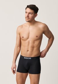Schwarze Boxer Briefs mit weißem "SNOCKS"-Logo auf dem elastischen Bund. Hergestellt aus einem glatten, dehnbaren Stoff, der sich dem Körper anpasst.