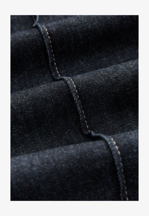 Melns džinsa audums ar gludu tekstūru un smalku spīdumu. Raksturo kontrastējošas brūnas šuves un viegli redzamas diagonālas pinuma rakstu līnijas.