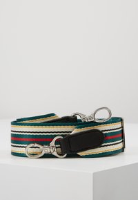 Pletený textilní řemínek v zelené, krémové a černé barvě s červenými a zlatými pruhy, vybavený kovovými karabinkami a koženými doplňky.