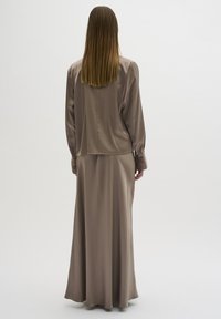 Lang, beige satin kjole med løs pasform, med samlet ærmer og en glat tekstur, der går ned under anklen.