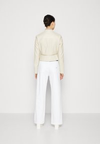 Veste en cuir beige raccourcie avec une coupe ajustée, associée à un pantalon blanc taille haute à jambes larges. Texture lisse, détails minimalistes.