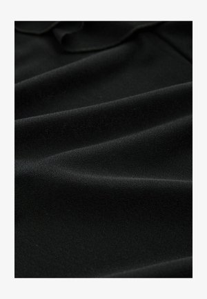 Melnā audumā ir gluda tekstūra, ar maigi plūstošām krokām. Materiāls šķiet viegls un nedaudz matēts.