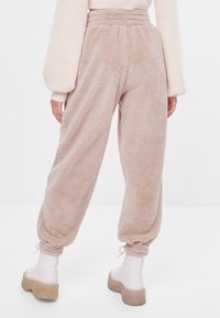 Fluffy beige joggingbroek met een elastische tailleband en gathered enkels, met een zachte textuur en een ontspannen pasvorm. Gedragen met witte plateau laarzen.