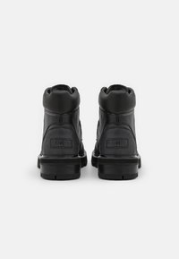 Svarta läderankelstövlar med en texturerad yta, vadderad krage och gummisulor, med en synlig logotyp på baksidan.