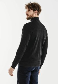 Maglione nero a collo alto con texture a coste sulle spalle, caratterizzato da un design elegante e indossato con jeans scuri.