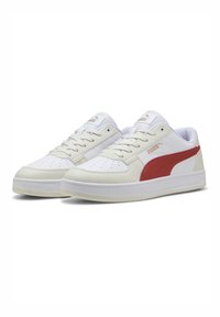 Hvide og røde sneakers med et glat læderoverdel, perforeret tåboks, snørebånd, polstret krave og en tekstureret gummisål.