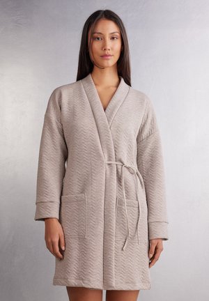 Beige texturerad kappa med ett chevronmönster, sjalkrage, långa ärmar, knytskärp i midjan och sidofickor. Mjuk tyg med en avslappnad design.