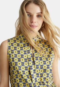 Top senza maniche con un motivo geometrico blu, giallo e bianco; scollatura a chiave, tessuto liscio e vestibilità comoda.