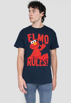 Navyblaues Baumwoll-T-Shirt mit einem großen roten Elmo-Logo, weißen Augen und einer orangefarbenen Nase, mit dem Text „ELMO REGIERT!“ in fetten roten Buchstaben.