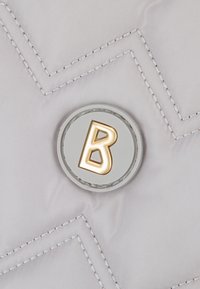 Tessuto grigio trapuntato con motivo a chevron, con una targhetta rotonda grigia al centro con la lettera "B" in oro.