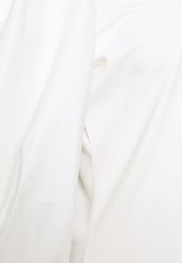 Vit bomullsskjorta med lång ärm och slät textur, med en enkel design och avslappnad passform. Inga synliga mönster eller detaljer.