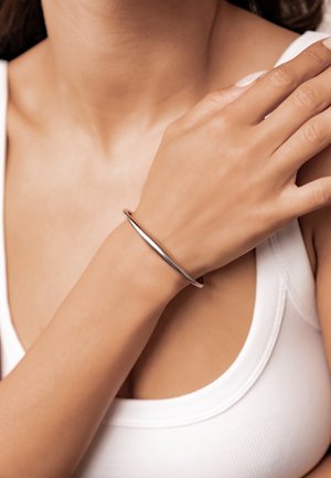 Silver metal bracelet with a smooth, round design. Worn on the wrist, the bracelet has a polished finish and a slight curve.