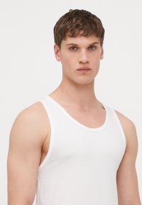 Weißes Baumwoll-Trägershirt mit breiten Trägern, Rundhalsausschnitt und taillierter Passform, ausgestattet mit einer glatten Textur und ohne sichtbare Muster.