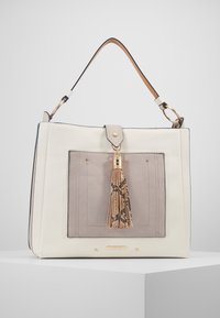 Vit läderhandväska med en beige framficka, guldfärgad metalldetalj och en dekorativ tofs med ormskinnsmönster. Robust handtag i toppen.