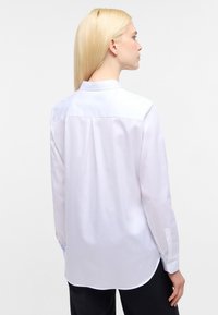 Hvid langærmet skjorte med lige snit, rygklap og knappede manchetter, lavet af glat stof. Skjorten har et klassisk kravedesign.