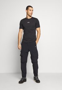 Sort T-shirt med korte ærmer og et lille logo på brystet, kombineret med mørke cargo-bukser med flere lommer og justerbare ærmer.