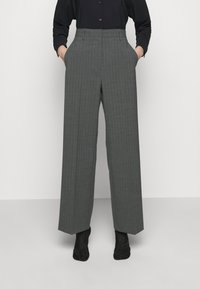 Šedé pruhované kalhoty s vysokým pasem a širokými nohavicemi, se bočními kapsami a hladkým povrchem. Černé boty doplňují celý look.