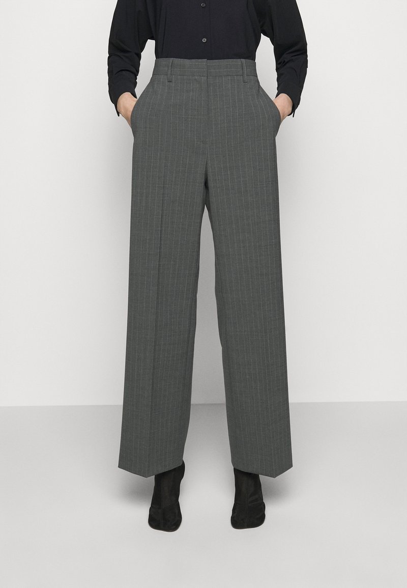 Šedé pruhované kalhoty s vysokým pasem a širokými nohavicemi, se bočními kapsami a hladkým povrchem. Černé boty doplňují celý look.