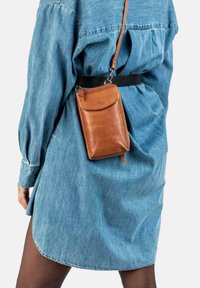 Person iført en blå denimkjole og sorte strømpebukser, med en lille brun læder crossbody taske hængende fra en skulderrem.