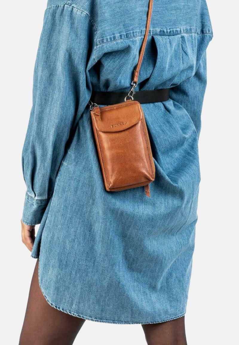 Person iført en blå denimkjole og sorte strømpebukser, med en lille brun læder crossbody taske hængende fra en skulderrem.