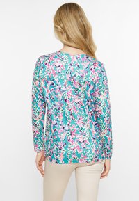 Blomstermønstret langærmet skjorte med turkis baggrund, accenter i pink, lilla og creme, der har en afslappet pasform og en rund bund.