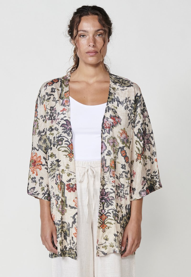 Chaqueta de kimono floral en tejido beige claro con patrones coloridos. Corte holgado, mangas anchas y diseño de frente abierto. Detalle de superficie texturizada.