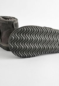 Grå mocka ankelboots med mjukt pälsfoder och en texturerad gummisula som har ett vågigt mönster. Enkelt design, lämplig för fritidsbruk.