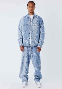 Conjunto de chaqueta y pantalones de denim con un patrón pixelado azul, cierre de botones y dos bolsillos en el pecho, combinado con zapatillas blancas.