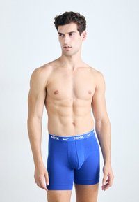 Nike blauwe boxershorts met een witte tailleband. Het materiaal lijkt glad en elastisch, ontworpen voor een nauwsluitende pasvorm om het lichaam.