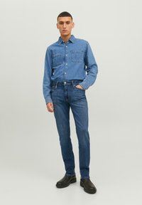Farmering ing két mellzsebbel, hosszú ujjal és galléros nyakkal, párosítva szűkített kék farmerral és fekete slip-on csizmával.