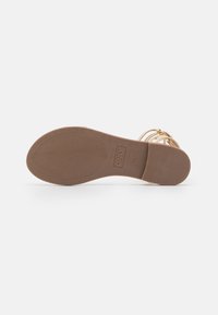 Litte tan sandaalin pohja, jossa on teksturoitu pito-ominaisuus ja brändi "ONLY" painettuna. Hihnat ovat metallinhohtoista kultaa minimalistisella muotoilulla.