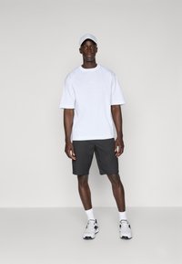Hvid kortærmet t-shirt med rund halsudskæring, parret med mørke shorts. Hvid kasket og grå sneakers fuldender det atletiske look.