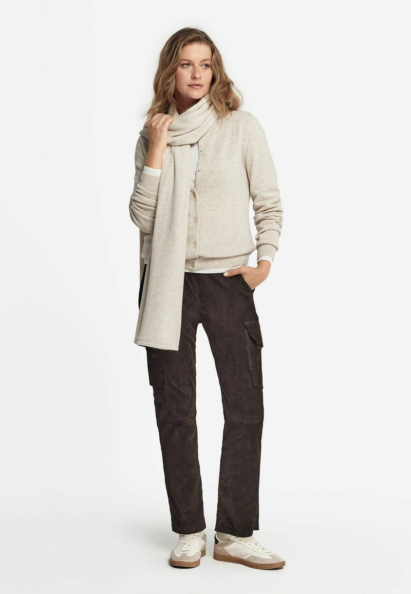 Cardigan beige clair avec des boutons, associé à un pantalon cargo marron foncé et des baskets blanches. L'écharpe est de la même couleur que le cardigan.