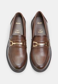 Mocassins en cuir marron au fini lisse, avec des accents en métal doré et une semelle intérieure Ortholite rembourrée pour le confort. Design classique avec un éclat subtil.