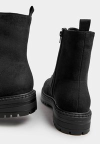 Stivali alla caviglia neri in suede con finitura texturizzata, cerniera laterale e una spessa suola in gomma nera con dettagli scanalati.