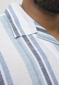 Camisa de manga corta en tejido ligero con rayas verticales en azul claro, azul oscuro y blanco, con un cuello puntiagudo y una superficie texturizada.